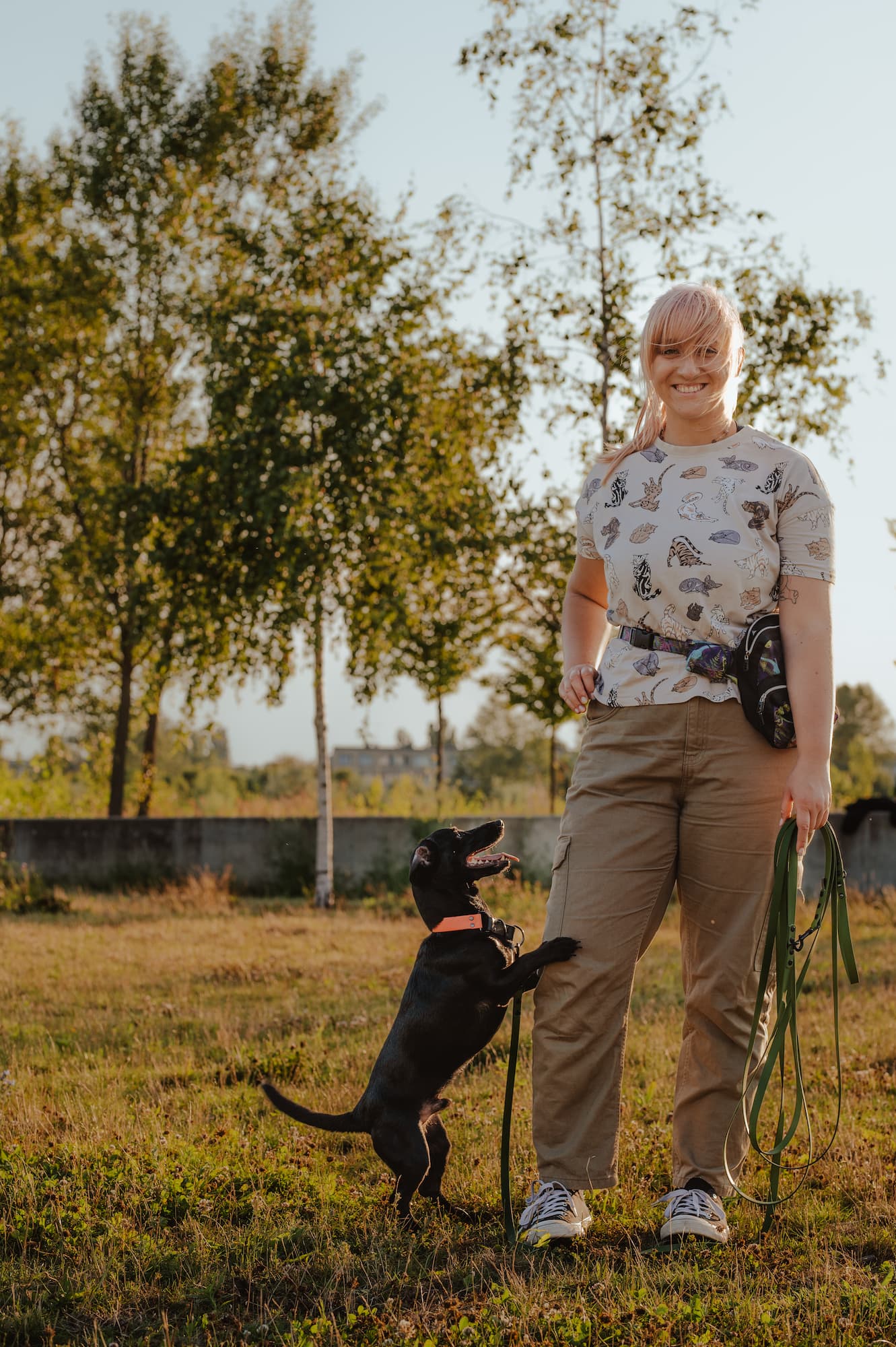 Uśmiechnięta trenerka psów Poznań trzyma smycz, czarny pies wspina się na jej nogę – pozytywne zakończenie sesji szkolenia posłuszeństwa